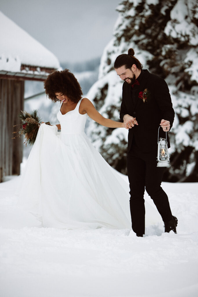 Braut und Bräutigam gehen Hand in Hand durch die verschneite Natur in der zauberhaften Bodenseeregion; der Bräutigam hält eine Laterne.
