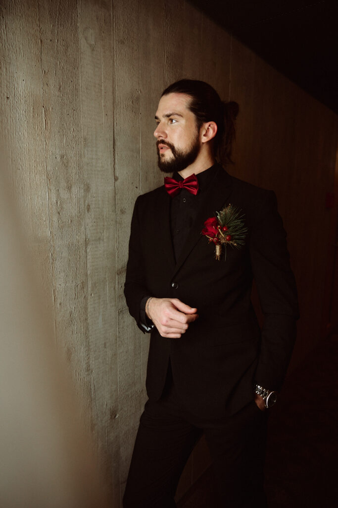 A man in a black suit with a red bow tie and corsage stands against a wooden wall and looks thoughtful, as if reflecting on memories from the Lake Constance region near the border between Austria and Switzerland.