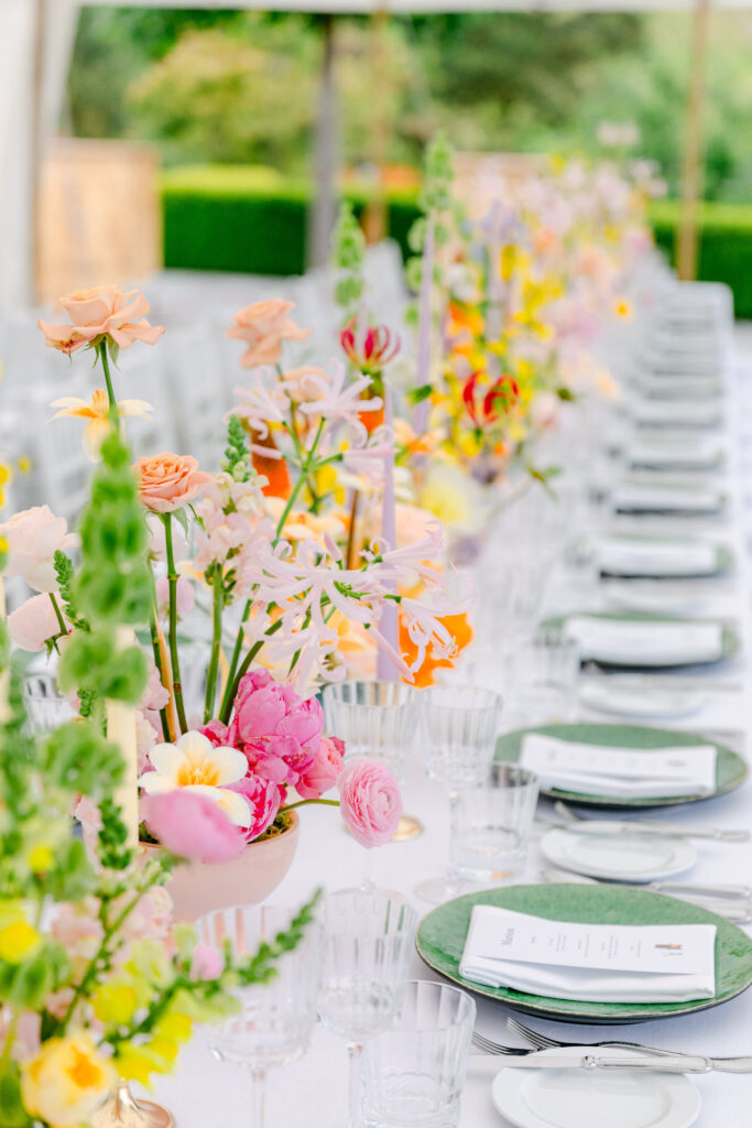 Ein langer Tisch ist mit grünen Tellern, Menüs und farbenfrohen Blumensträußen bei einem Hochzeitswochenende im Freien in der malerischen Bodenseeregion gedeckt.